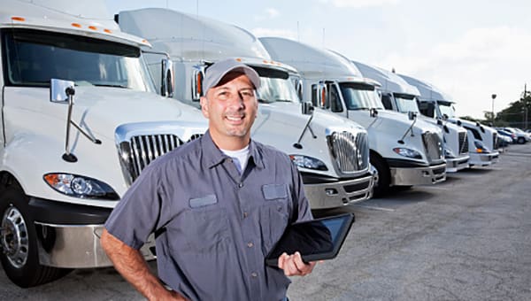 Truck driver in front of big rigs with digital tablet