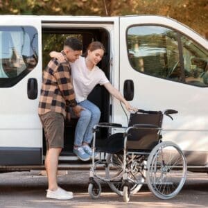 Man helping a woman out of a van and into a wheelchair.