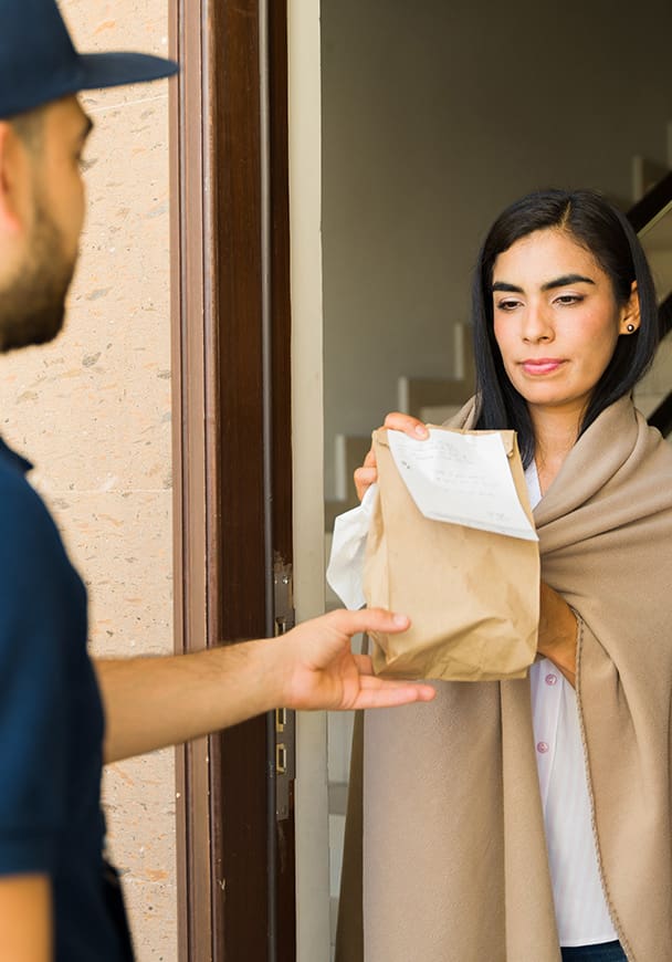 A woman at her door wrapped in a blanket accepting a delivery for medication