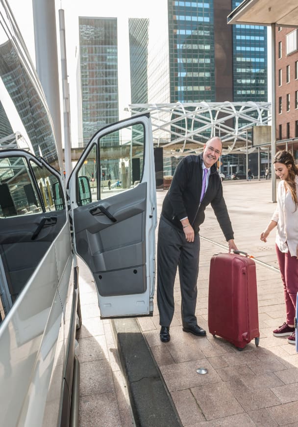 A man at the airport helping passengers get their luggage into a sprinter van
