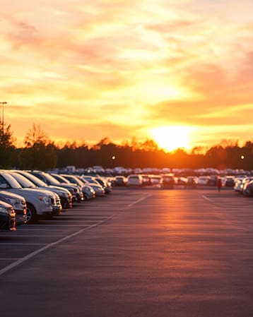 A sunset landscape with a parking lot filled with vehicles ouside a manufacturing building
