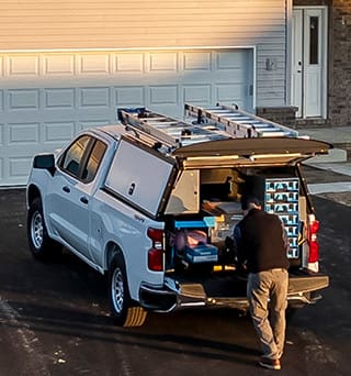 A truck in front of a home upfitted with cabinets in the flatbed cap