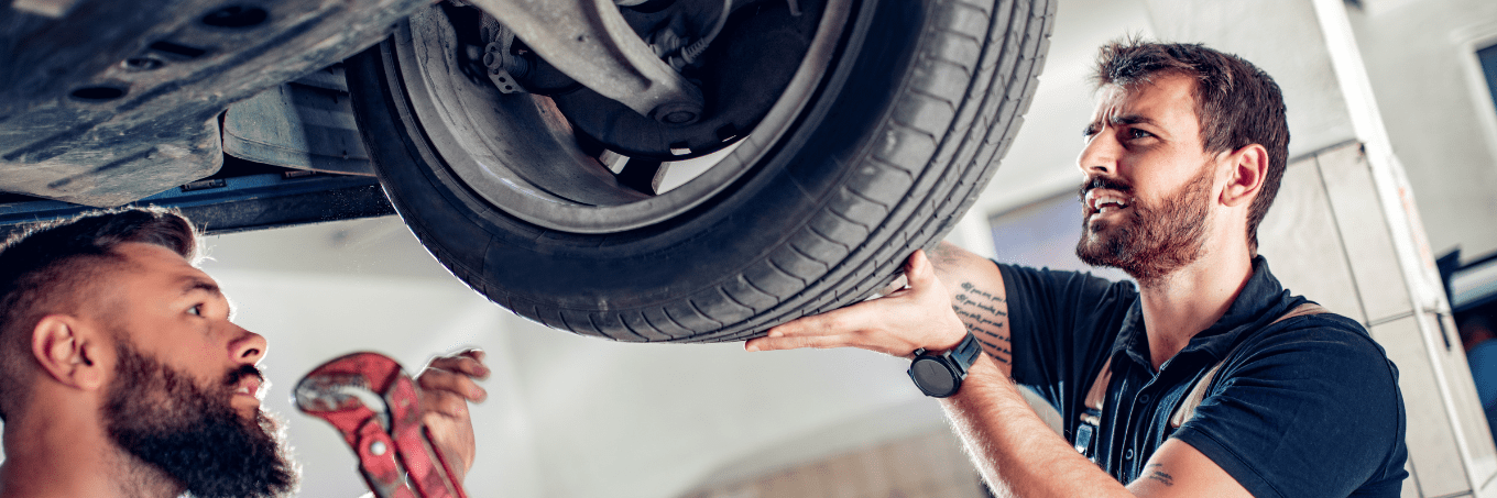 Two mechanics looking at a tire underneath a car. Capital Lease group provides full maintenance services for our leased cars and trucks and leased vans